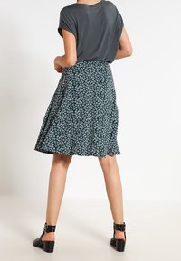 Jupe évasée à fleurs de couleur vert foncé avec un motif bleu ; tissu léger. Assortie à un haut gris et des sandales à talons carrés noires.
