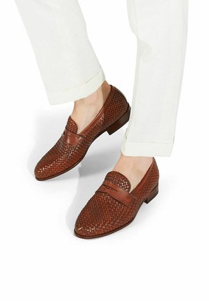 Braune gewebte Lederloafers mit abgerundetem Zehenbereich und niedrigem Absatz, kombiniert mit weißen knöchellangen Hosen. Mit dezenten Lederakzenten.