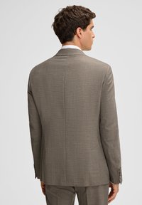 Brązowa marynarka z tweedu, dopasowany krój, pojedyncze rozcięcie z tyłu oraz cztery guziki ozdobne na mankietach. Gładka faktura z subtelnym wzorem.