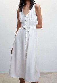 Valkoinen without sleeveli mekko, jossa on V-pääntie, nappisulku edessä ja sidottava vyötärö. Ominaisuuksiin kuuluu ilmava muotoilu ja sileä pinta.