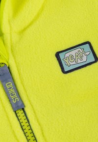 Lime green fleece jacket with a zip closure, featuring a blue rectangular patch with "YEAH" text and a gray label with "SIGIKID."