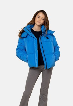 Blauwe pufferjack met een capuchon, voorzien van een ritssluiting aan de voorkant, drukknoopjes en gestikte panelen. Draag het over een zwart topje en gestreepte broek.