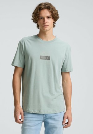 Light mint green cotton t-shirt with short sleeves, crew neckline, and a subtle white and grey printed logo on the front.