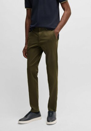 Chinos verde oliva realizzati in misto cotone, con una vestibilità slim e tasche laterali, abbinati a sneakers blu navy con accenti bianchi.