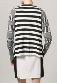 Cárdigan de punto a rayas en blanco y negro con mangas largas, dobladillo redondeado y anchos de rayas variables, superpuesto a una falda en blanco y negro.
