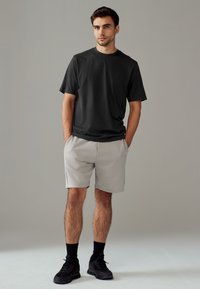 Maglietta nera in cotone, vestibilità comoda, abbinata a pantaloncini grigio chiaro. Calzini neri e scarpe da ginnastica. Design semplice, colori neutri. Trame lisce.