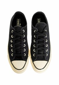Sneakers in tessuto nero con finitura texturizzata, punta in gomma bianca e lacci neri. Presentano occhielli argentati e suola beige con strisce nere.