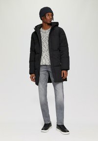 Schwarze gepolsterte Jacke mit Kapuze, grauer gemusterter Pullover, hellgraue Jeans und schwarze Sneaker. Glatte Textur und einfaches Design.