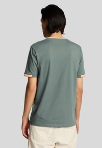 Grøn bomulds T-shirt med korte ærmer, ribbet rund hals og orange detaljer ved ærmeenderne. Glat tekstur, afslappet pasform.