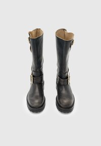 Botas de cuero negro hasta la rodilla con punta redonda, correas con hebilla y suela robusta. Textura suave con un forro beige contrastante.