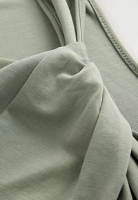 Tissu vert avec un tissage texturé, présentant des éléments de design noués et une drape douce, mettant en valeur sa qualité lisse et extensible.