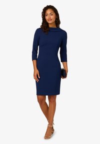 Granatowa sukienka z dekoltem łódka, rękawami o długości trzech ćwierć i dopasowanym krojem. Gładki materiał z pionowymi szwami na detalach.