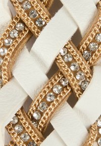 Cinghie intrecciate bianche con accenti dorati e strass chiari intrecciati, che mettono in mostra una superficie testurizzata e dettagli scintillanti.