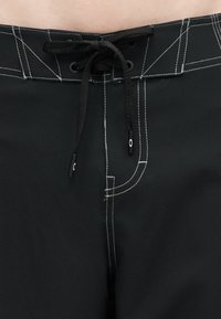 Μαύρο μαγιό βερμούδα με λευκά ραφικά σημεία αντίθεσης και μαύρο κορδόνι δέσιμο στη μέση.