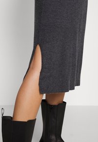 Szara dzianinowa spódnica midi z bocznym rozcięciem, gładką fakturą i prążkowanym wykończeniem. Połączona z czarnymi, skórzanymi botkami za kolano.