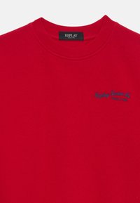 Roter Baumwoll-Sweatshirt mit rundem Ausschnitt. Verfügt über den blauen gestickten Text "Replay Denim Co. Seit 1981" auf der Vorderseite. Glatte Textur, lässiges Design.