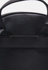 Bolso de mano de cuero negro con textura de grano, acentos cosidos y una etiqueta rectangular de marca con la inscripción "Michael Kors" en relieve.