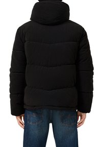 Giubbotto puffer in corduroy nero con cappuccio, caratterizzato da sezioni a righe orizzontali cucite e cuciture a contrasto. Indossato sopra jeans blu.