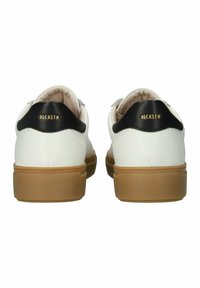 Sneaker bianchi in pelle con tallone nero e suola in gomma beige. Branding in oro ben visibile sul tallone. Texture liscia.