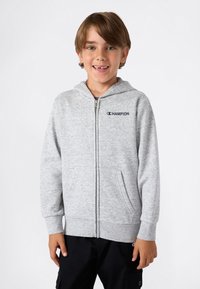 Sudadera gris con cremallera hecha de tejido texturizado, que presenta un bolsillo tipo canguro y un pequeño logo en la parte izquierda del pecho.