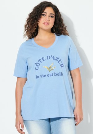 T-shirt bleu clair à manches courtes en V en tissu doux, comportant le texte "CÔTE D'AZUR la vie est belle" avec un motif floral.