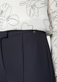 Blus med blommönster i vitt med svarta konturer, parat med mörkblå strukturerade byxor med flat front och subtila detaljer.