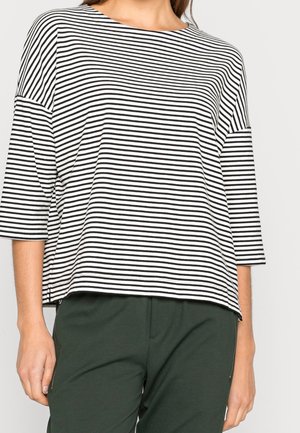 Person wearing a black and white horizontal striped long sleeve top with dark green pants, shown from neck to hips.