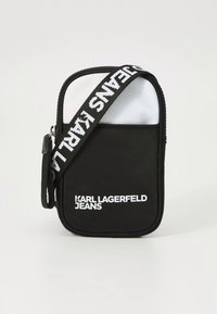 Črno-bela torbica čez ramo z gladko teksturo, ki ima izpostavljen logotip, kontrastni panel in nastavljiv trak.