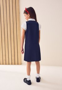 Dunkelblaues Schulkleid mit plissiertem Rock, weißem Kragenhemd und schwarzen Schuhen mit weißen Rüschensocken. Ein rotes Haarband rundet den Look ab.