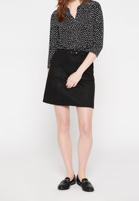 Czarna spódnica o dopasowanym kroju z dwoma przednimi kieszeniami, połączona z czarną bluzką w groszki z rękawami do łokcia.