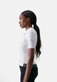 Weißes Sportshirt mit kurzen Ärmeln, gerippter Textur und grauem Saum am unteren Ende. Matte Oberfläche mit einem Logo nahe dem Hals.