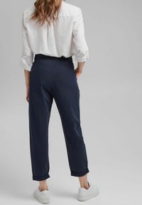 Pantalon bleu marine à coupe décontractée, avec ourlets retroussés et poches arrière, associé à une chemise blanche boutonnée et des baskets blanches.