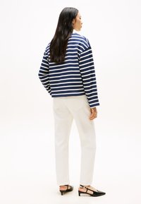 Top a righe blu navy e bianco, design cropped, abbinato a pantaloni bianchi e décolleté nere con cinturino, visto da dietro.