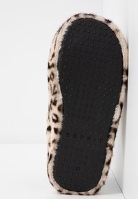 Semelle unique de pantoufle en caoutchouc noir avec grip texturé, entourée d'une doublure en fourrure douce à imprimé léopard sur fond blanc.