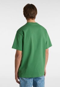 T-shirt in cotone verde con maniche corte, collo rotondo e vestibilità comoda, abbinato a jeans azzurri chiari con motivi a fiamma.