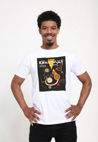 Bílý bavlněný tričko s grafickým potiskem s abstraktními tvary v černé, žluté, oranžové, červené a modré. Text zní "KANDINSKY."