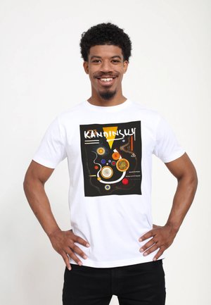 Bílý bavlněný tričko s grafickým potiskem s abstraktními tvary v černé, žluté, oranžové, červené a modré. Text zní "KANDINSKY."
