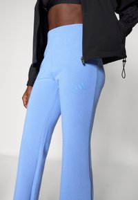 Svetlo modri atletski hlače z gladko teksturo, prilegajoče se v pasu in razširjene na dnu. Imajo diskreten embosiran logotip na strani.