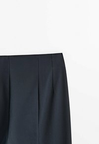 Pantalons ajustés bleu foncé au texture lisse, avec un devant plat, des plis et une ceinture propre, mettant en avant un design minimaliste.