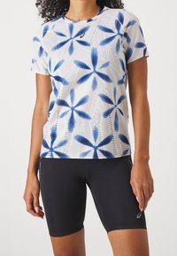 Short-sleeve athletic t-shirt in white with blue flower patterns, paired with black fitted shorts, featuring breathable mesh texture.