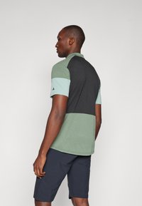 Polo de manga corta con un diseño en bloques de color verde y negro, confeccionado en una tela ligera con un acabado texturizado.