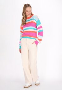 Maglione a righe multicolore nei colori rosa, arancione, blu e bianco. Vestibilità comoda con scollatura rotonda. Abbinato a pantaloni a gamba larga color crema e sneakers bianche.