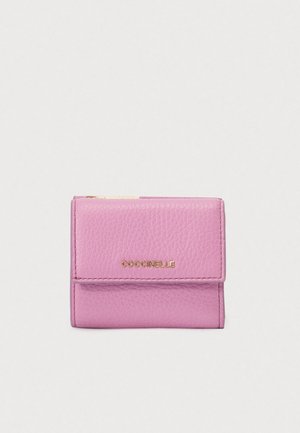 Compact pink leather wallet with textured surface, gold zipper, and "COCCINELLE" logo on front flap against white background.