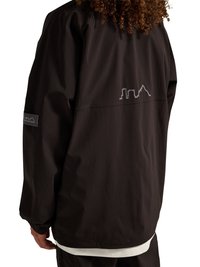 Person med krøllet hår iført en sort jakke med reflekterende by-silhuetlogoer på øvre ryg og venstre ærme.