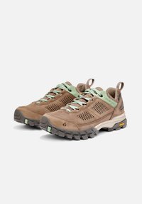 Scarpe da trekking basse marroni e verdi con pannelli in rete, suole spesse e scolpite, e linguette di pull su uno sfondo bianco.