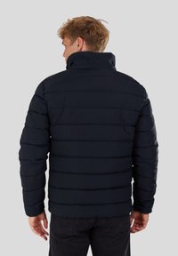 Marineblaue Steppjacke mit hohem Kragen, horizontal gestepptem Design und weicher Textur, mit lockerer Passform und ohne sichtbare Verschlüsse.