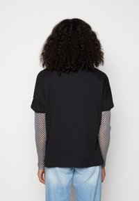 T-shirt nero a maniche corte sovrapposto a una maglia a maniche lunghe a rete a quadri, abbinato a jeans di denim azzurri.