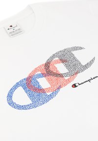 Camiseta de algodón blanca con un diseño gráfico de logotipos en forma de "C" superpuestos en rojo, azul y negro. Incluye la marca "Champion" en cursiva.