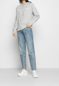 Sudadera gris de algodón con cordones y logo blanco, combinada con jeans de denim azul claro y zapatillas blancas con suelas texturizadas.
