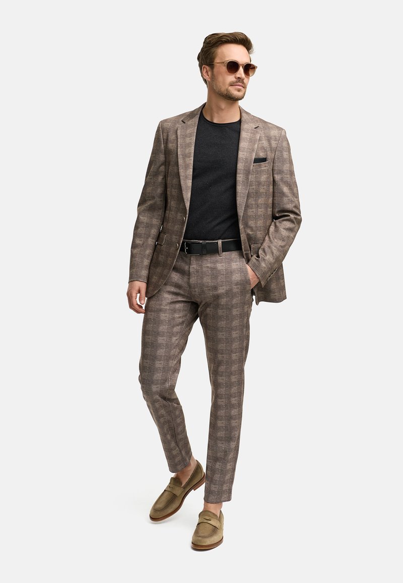 Braun kariertes Anzug aus strukturiertem Stoff, kombiniert mit einem schwarzen Hemd und hellbraunen Loafers. Beinhaltet Sonnenbrille und ein Einstecktuch.